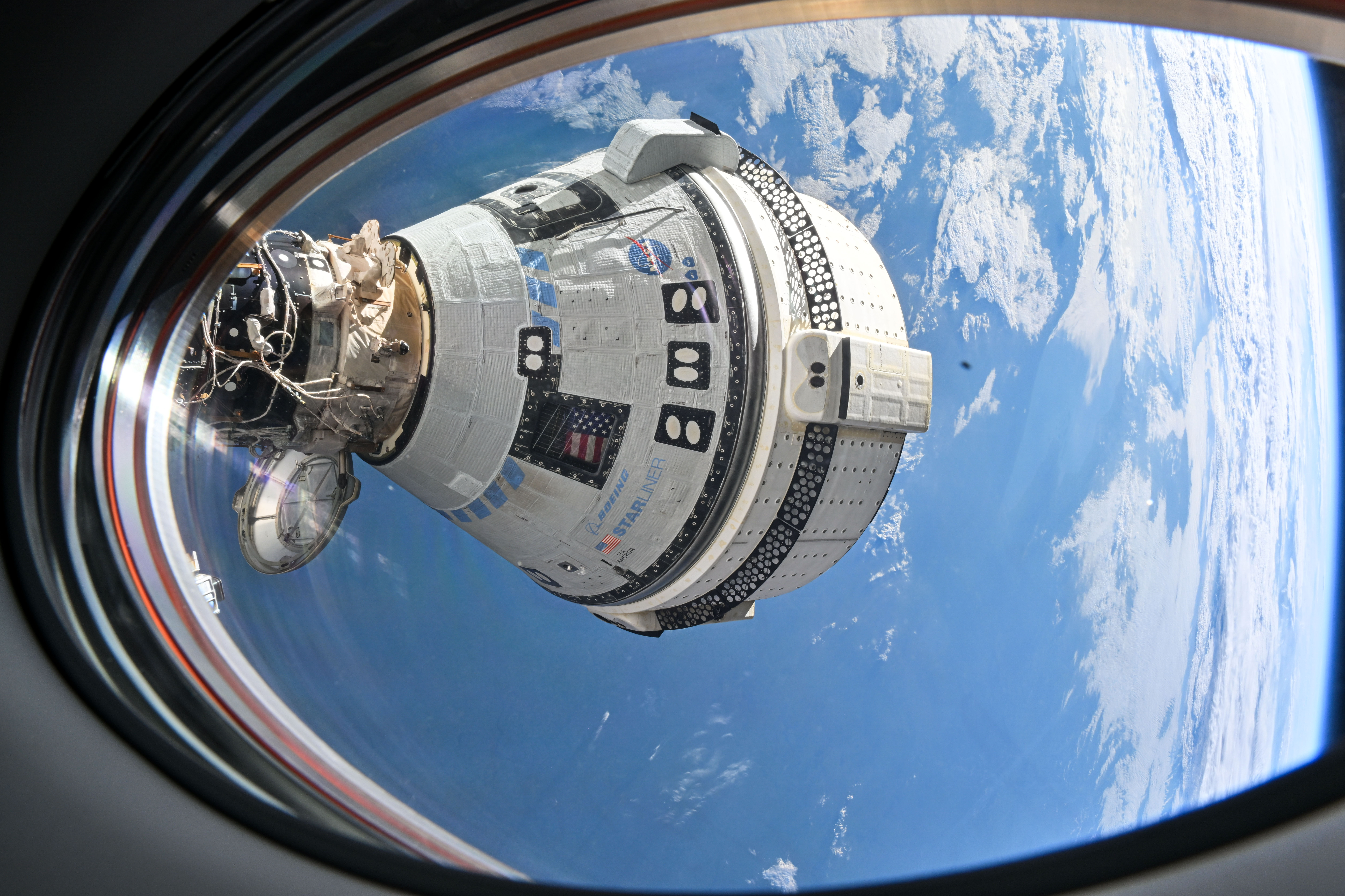 La navicella Starliner alla Stazione Spaziale Internazionale vista dal finestrino di una Crew Dragon